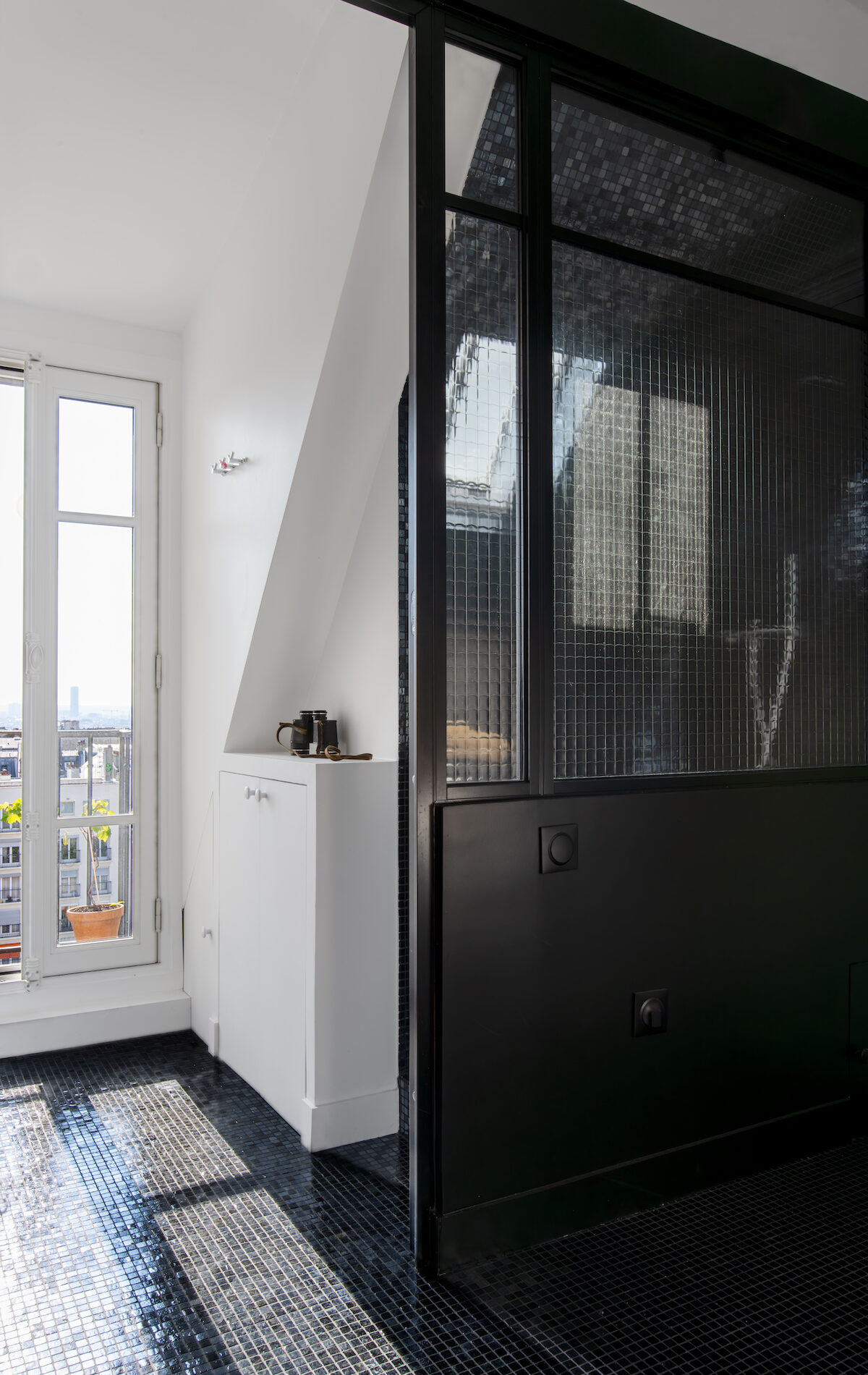Verrière intérieure noire structurant l’espace dans un studio sous les toits
